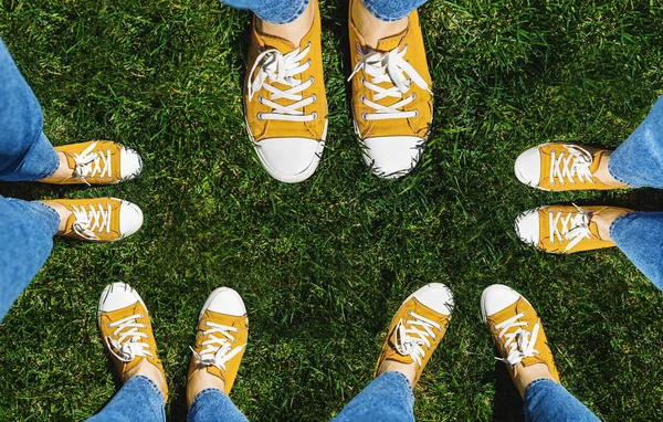 Collage of legs in old yellow sneakers on green grass. View from above. The concept of youth, spring and freedom. Isolated on white background.