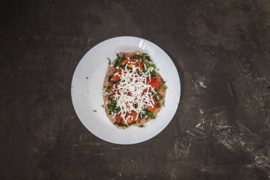 Fileto tavuk otlar ile pişirme için hazırlanan, domates, peynir peynir karanlık bir beton zemin üzerine beyaz bir tabakta. Yukarıdan görüntüleyin. Sağlıklı doğru beslenme kavramı. Minimalizm. Düz yatıyordu.