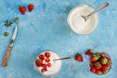Organik yoğurt bir kase taze çilek mavi bir beton zemin üzerinde kesti. Üstten görünüm ve yakın çekim. Flatlay.