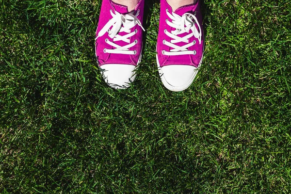 Legs in old pink sneakers on green grass. View from above. The concept of youth, spring and freedom.