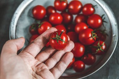 el seçer ve bir kevgir içinde bütün taze kiraz domates gösterir.