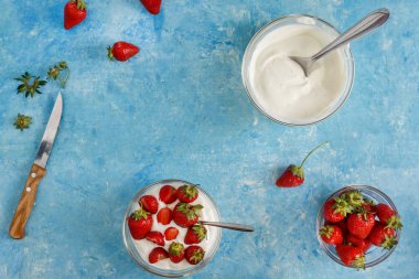 Organik yoğurt bir kase taze çilek mavi bir beton zemin üzerinde kesti. Üstten görünüm ve yakın çekim. Flatlay.
