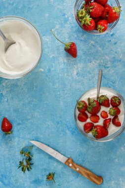 Organik yoğurt bir kase taze çilek mavi bir beton zemin üzerinde kesti. Üstten görünüm ve yakın çekim. Flatlay.