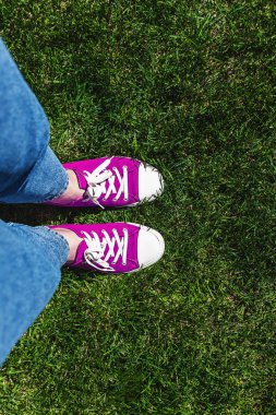 Yeşil çimenlerin üzerinde eski pembe spor ayakkabılar bacaklar. Yukarıdan görüntüleyin. Gençlik, bahar ve Özgürlük kavramı.