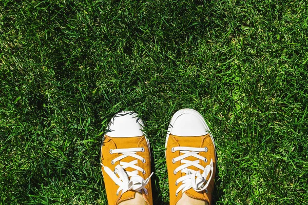 Legs in old yellow sneakers on green grass. View from above. The concept of youth, spring and freedom.
