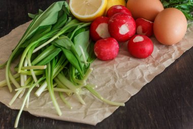 Parşömen kağıt üzerine koyu arka plan üzerinde bir tencerede salata, yabani sarımsak, turp, limon, urkop, tavuk yumurtası için hazırlanan taze sebze ve ürün, sos