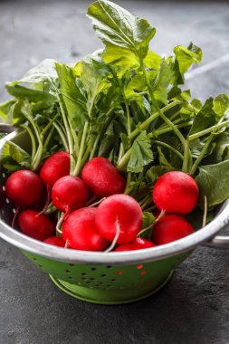 Karanlık bir arka plan üzerinde bir kevgir içinde yıkanmış taze sulu kırmızı turp