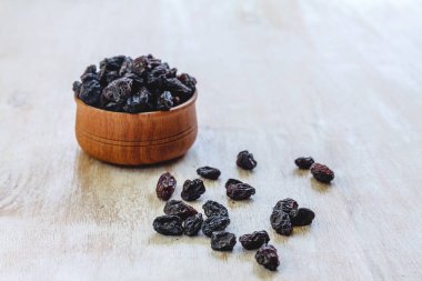 Parlak beyaz bir arka plan üzerinde ahşap bir kapta koyu mavi kuru üzüm.