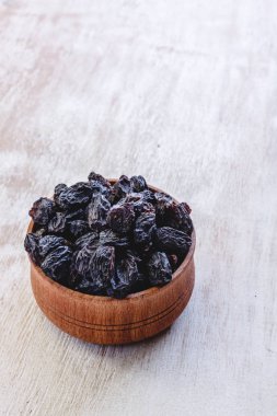 Parlak beyaz bir arka plan üzerinde ahşap bir kapta koyu mavi kuru üzüm.