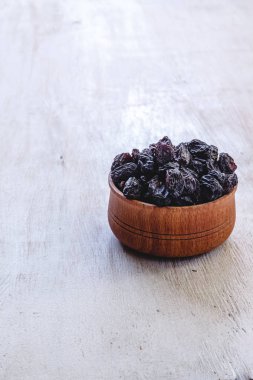 Parlak beyaz bir arka plan üzerinde ahşap bir kapta koyu mavi kuru üzüm.