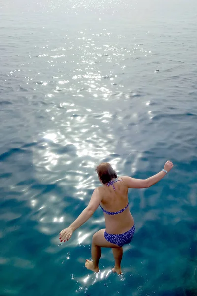 Young woman girl in a blue bathing suit jumping in the water-sea — Stock Photo, Image