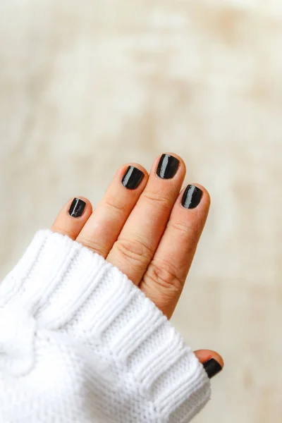 Mano con manicura negra en uñas cortas en un suéter blanco en un —  Fotos de Stock