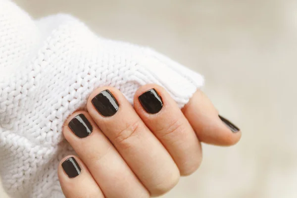 Hand met zwarte manicure op korte nagels in een witte trui op een — Stockfoto