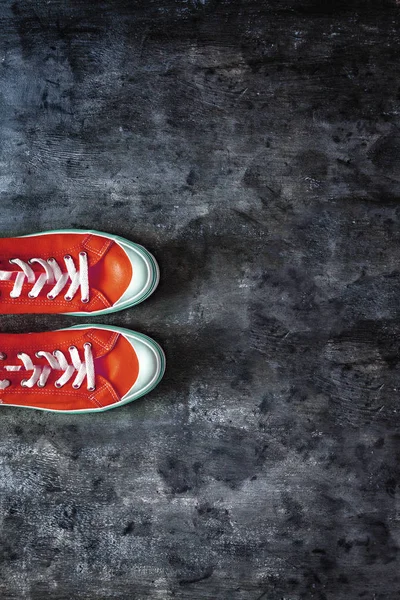 red sneakers with untied laces on a dark concrete background. Co