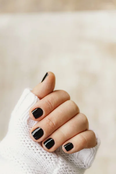 Mano con manicura negra en uñas cortas en un suéter blanco en un — Foto de Stock