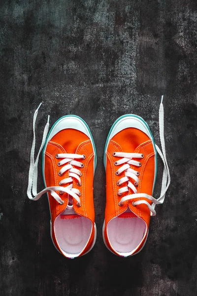 red sneakers with untied laces on a dark concrete background. Co