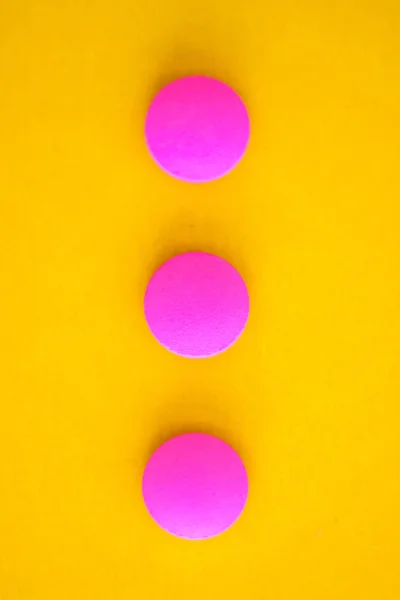 Composición de tres píldoras redondas de color rosa sobre un fondo amarillo. Fl — Foto de Stock