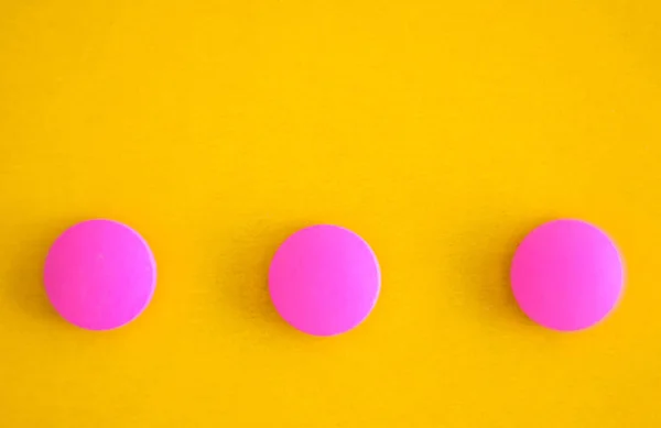 Composición de tres píldoras redondas de color rosa sobre un fondo amarillo. Acostado. Copiar espacio. Tendencia Primer plano — Foto de Stock