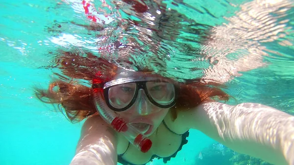 Young woman girl makes selfie, takes pictures of herself under water in the sea, near the coral reefs