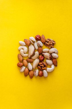 Fındık çeşitli sarı bir arka planda bir daire şeklinde dışarı yerleştirilir. Düz yatıyordu. Yukarıdan görüntüle. Boşluk Kopyala. Sağlık, kardiyo, uygun beslenme, sağlıklı yağlar kavramı