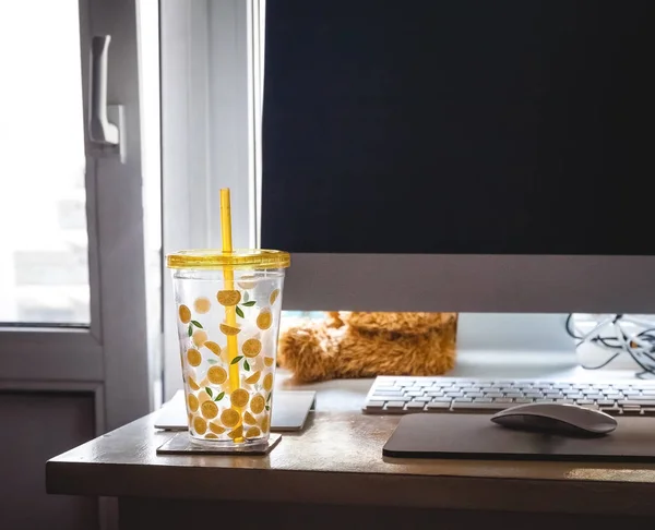 Szklankę ze słomką z malowanymi cytryniami na biurku domowego biura w pobliżu komputera — Zdjęcie stockowe