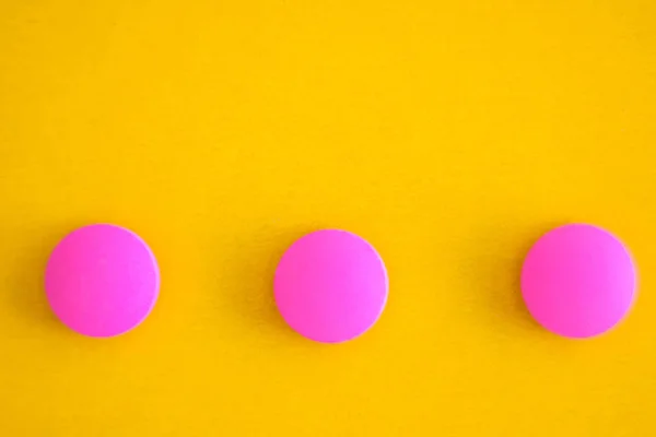 Composición de tres píldoras redondas de color rosa sobre un fondo amarillo. Acostado. Copiar espacio. Tendencia Primer plano — Foto de Stock