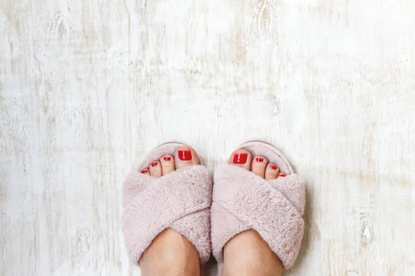 Female legs with red nails in home fur fluffy pink slippers on a light wooden background. flat lay. Top view. The concept of a cozy bright girl house — Stock Photo, Image