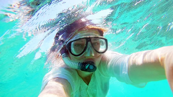 Young woman girl makes selfie, takes pictures of herself under water in the sea, near the coral reefs
