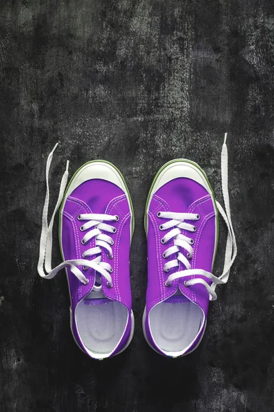 purple-pink-lilac sneakers with untied laces on a dark concrete background. Copy space. View from above.
