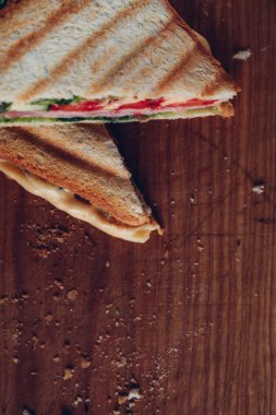 Ahşap arka planda iki sandviç, üst görünüm. Bir kesme tahtasında jambon, peynir ve marul sandviç ile Panini yığını