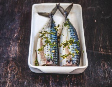 Yeşiller ve otlar iki çiğ balık uskumru karanlık bir arka planda pişmiş olacak. Yukarıdan görüntüle. Retro etkisi