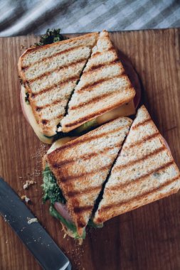 Ahşap arka planda iki sandviç, üst görünüm. Bir kesme tahtasında jambon, peynir ve marul sandviç ile Panini yığını
