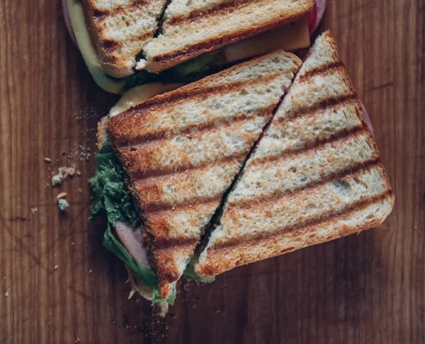 Two sandwiches on a wooden background, top view. Stack of panini with ham, cheese and lettuce sandwich on a cutting board — Stock Photo, Image