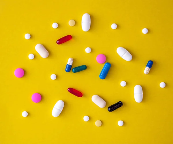 Spridda en mängd flerfärgade piller i en gul-orange bakgrund. Utsikt från ovan. Närbild — Stockfoto