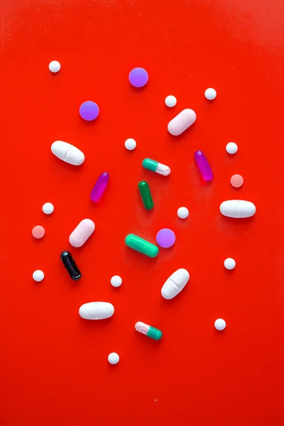 Piros háttéren különböző színű tablettákat szórtak. Kilátás fentről. Közeli — Stock Fotó