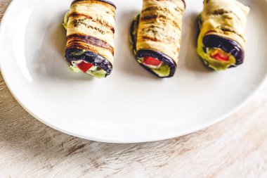 hafif bir arka plan üzerinde beyaz bir tabak üzerinde kızarmış patlıcan, süzme peynir ve domates geleneksel çanak üç rulo. Minimalizm. Yukarıdan görüntüle