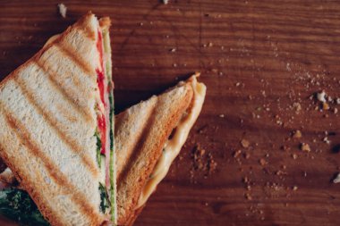 Ahşap arka planda iki sandviç, üst görünüm. Bir kesme tahtasında jambon, peynir ve marul sandviç ile Panini yığını
