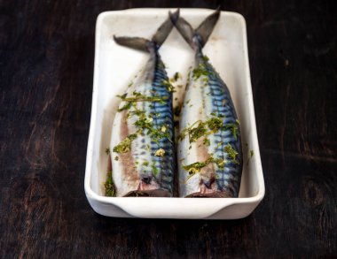 Yeşiller ve otlar iki çiğ balık uskumru karanlık bir arka planda pişmiş olacak. Yukarıdan görüntüle. Retro etkisi