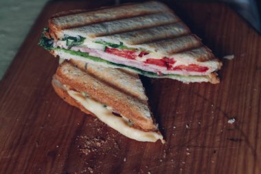 Ahşap arka planda iki sandviç, üst görünüm. Bir kesme tahtasında jambon, peynir ve marul sandviç ile Panini yığını