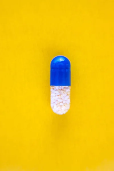 Eine blaue Pillenkapsel isoliert auf gelbem Hintergrund, Nahaufnahme, Draufsicht, Kopierraum — Stockfoto
