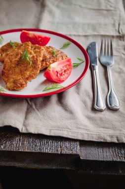 sulu et-tavuk pirzola ve basit bir hafif keten arka plan üzerinde beyaz bir tabak üzerinde domates çatal ve bıçak ile servis