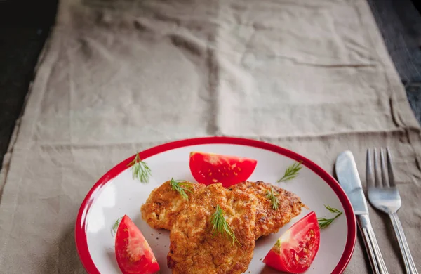 フォークとナイフを添えたシンプルなライトリネンの背景に白いプレートにジューシーな肉チキンチョップとトマト — ストック写真