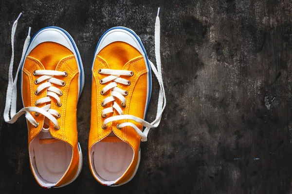 yellow-orange sneakers with untied laces on a dark concrete background. Copy space. View from above.