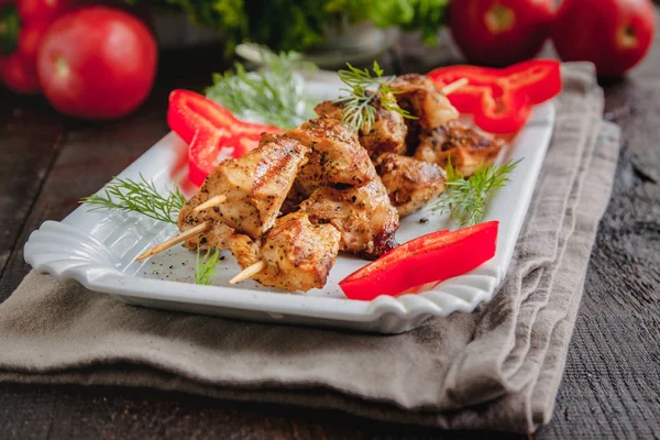 juicy meat-chicken skewers on wooden skewers on a white plate on a dark wooden background