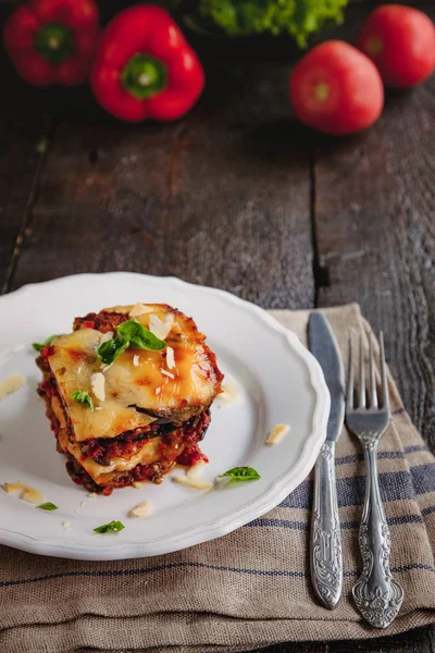 Tradizionale Parmigiana di melanzane: melanzane al forno - Italia, cucina siciliana.Melanzane al forno con formaggio, pomodori e spezie su un piatto bianco. Un piatto di melanzane è su un tavolo di legno — Foto Stock