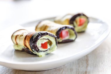 hafif bir arka plan üzerinde beyaz bir tabak üzerinde kızarmış patlıcan, süzme peynir ve domates geleneksel çanak üç rulo. Minimalizm. Yukarıdan görüntüle