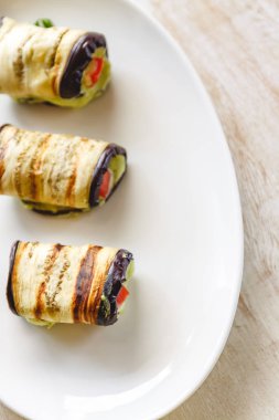 hafif bir arka plan üzerinde beyaz bir tabak üzerinde kızarmış patlıcan, süzme peynir ve domates geleneksel çanak üç rulo. Minimalizm. Yukarıdan görüntüle