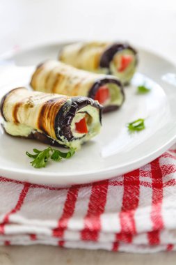 hafif bir arka plan üzerinde beyaz bir tabak üzerinde kızarmış patlıcan, süzme peynir ve domates geleneksel çanak üç rulo. Minimalizm. Yukarıdan görüntüle