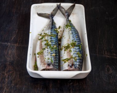Yeşiller ve otlar iki çiğ balık uskumru karanlık bir arka planda pişmiş olacak. Yukarıdan görüntüle. Retro etkisi