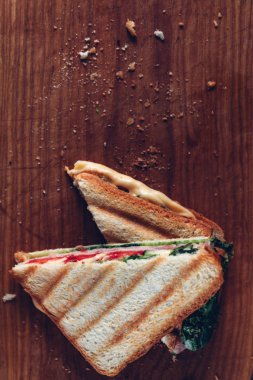Ahşap arka planda iki sandviç, üst görünüm. Bir kesme tahtasında jambon, peynir ve marul sandviç ile Panini yığını